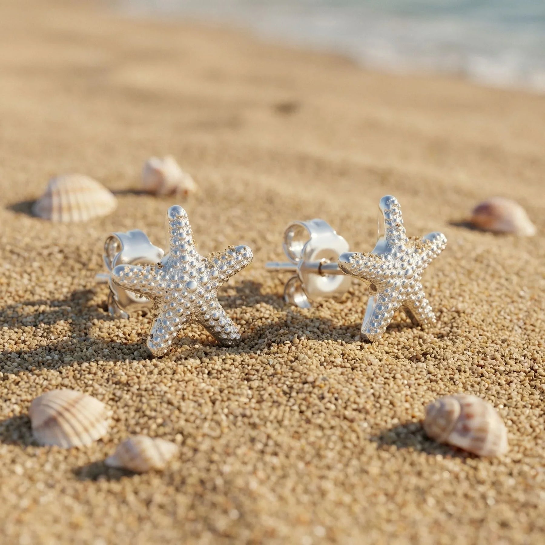 Silberne Seestern Ohrstecker auf Sandstrand mit Muscheln, maritimer Schmuck