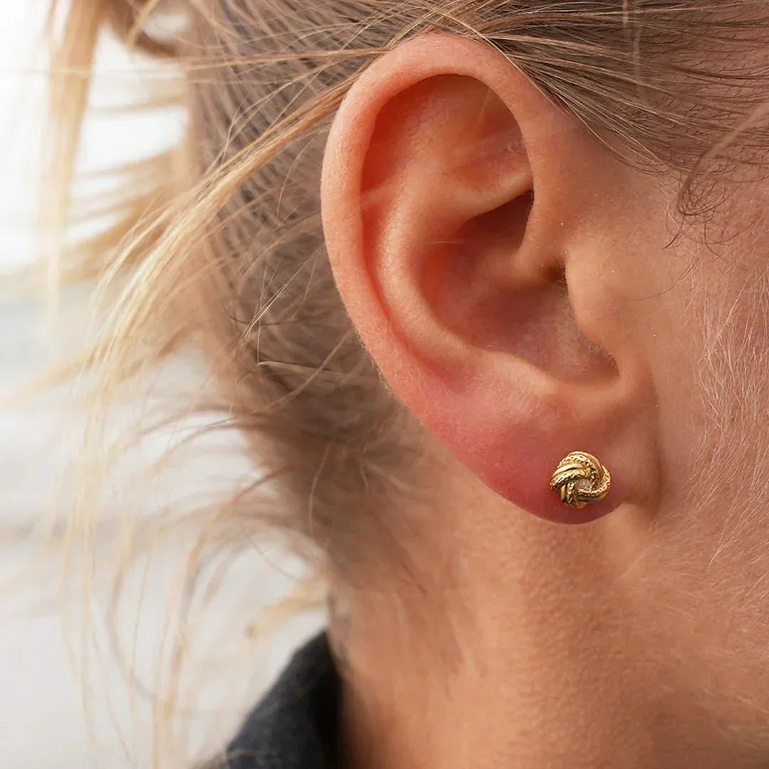 Nahaufnahme eines Ohrs mit goldenen Knoten-Ohrsteckern, maritimer Schmuckstil