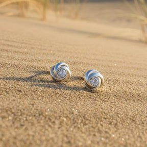 Silberne Ohrstecker in Knotenform mit Zirkonia auf Sand am Strand, maritimer Schmuck