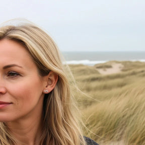 Frau mit silbernem Wellen-Ohrstecker am Strand, maritimer Schmuck, Dünen im Hintergrund