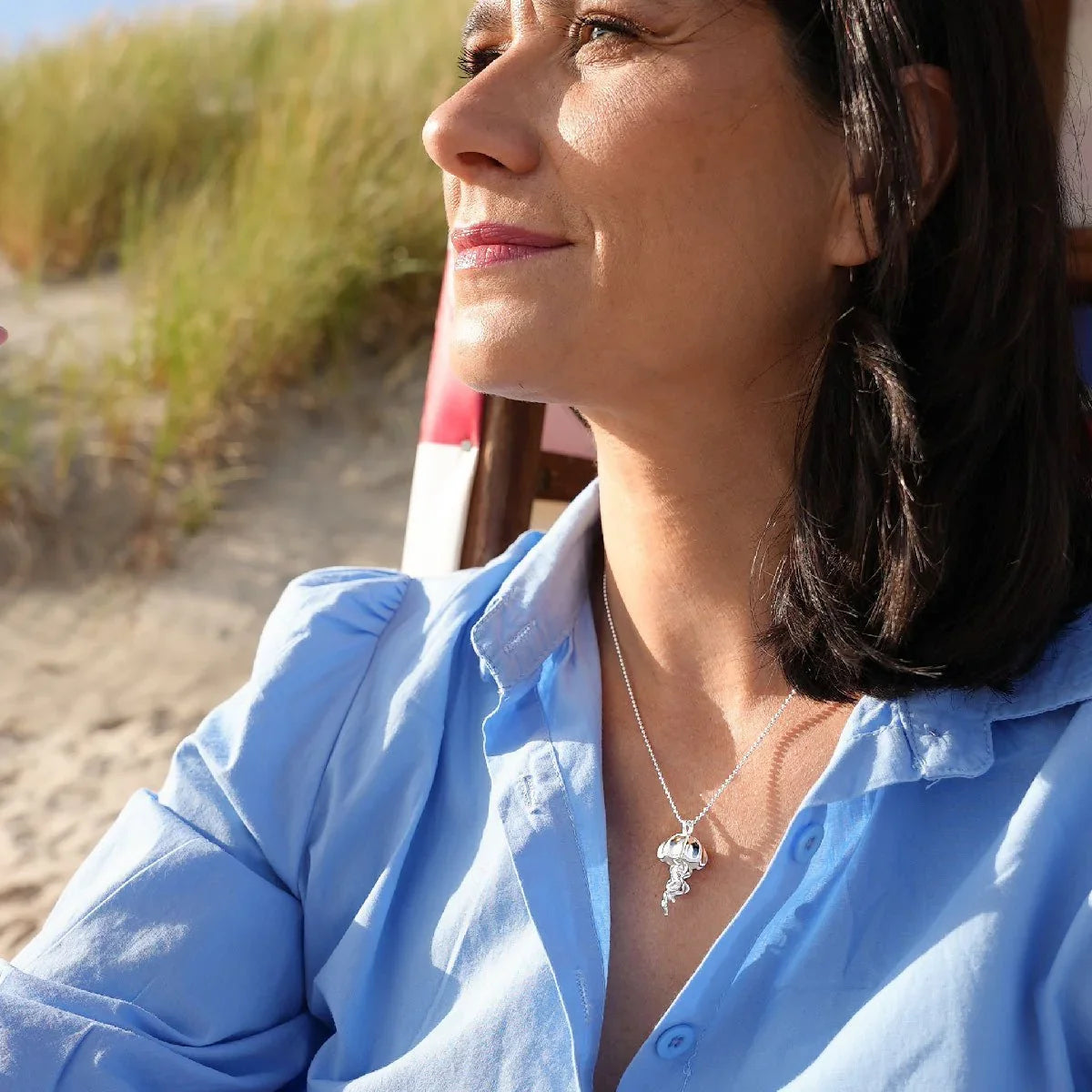 Frau am Strand mit Silberkette und Quallen-Anhänger, maritimer Schmuck im Sonnenlicht