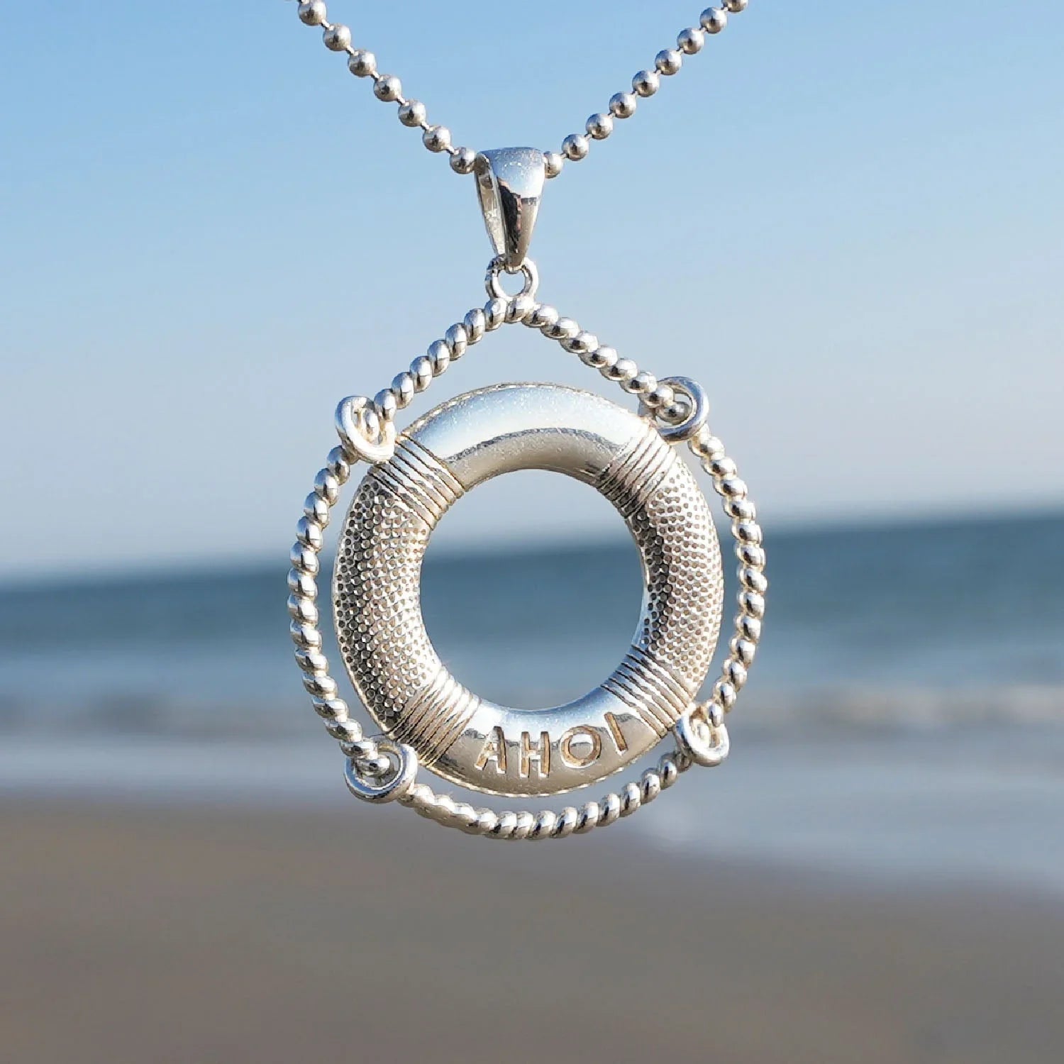 Silberner Rettungsring-Anhänger mit Gravur AHOI, maritimer Schmuck am Strand vor dem Meer