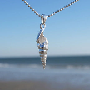 Silberner Muschel-Anhänger an Kette, maritimer Schmuck vor Meer und blauem Himmel