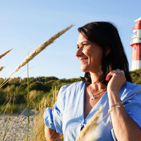 Frau am Strand mit maritimem Schmuck, Anhänger Schildkröte Silber, Leuchtturm im Hintergrund