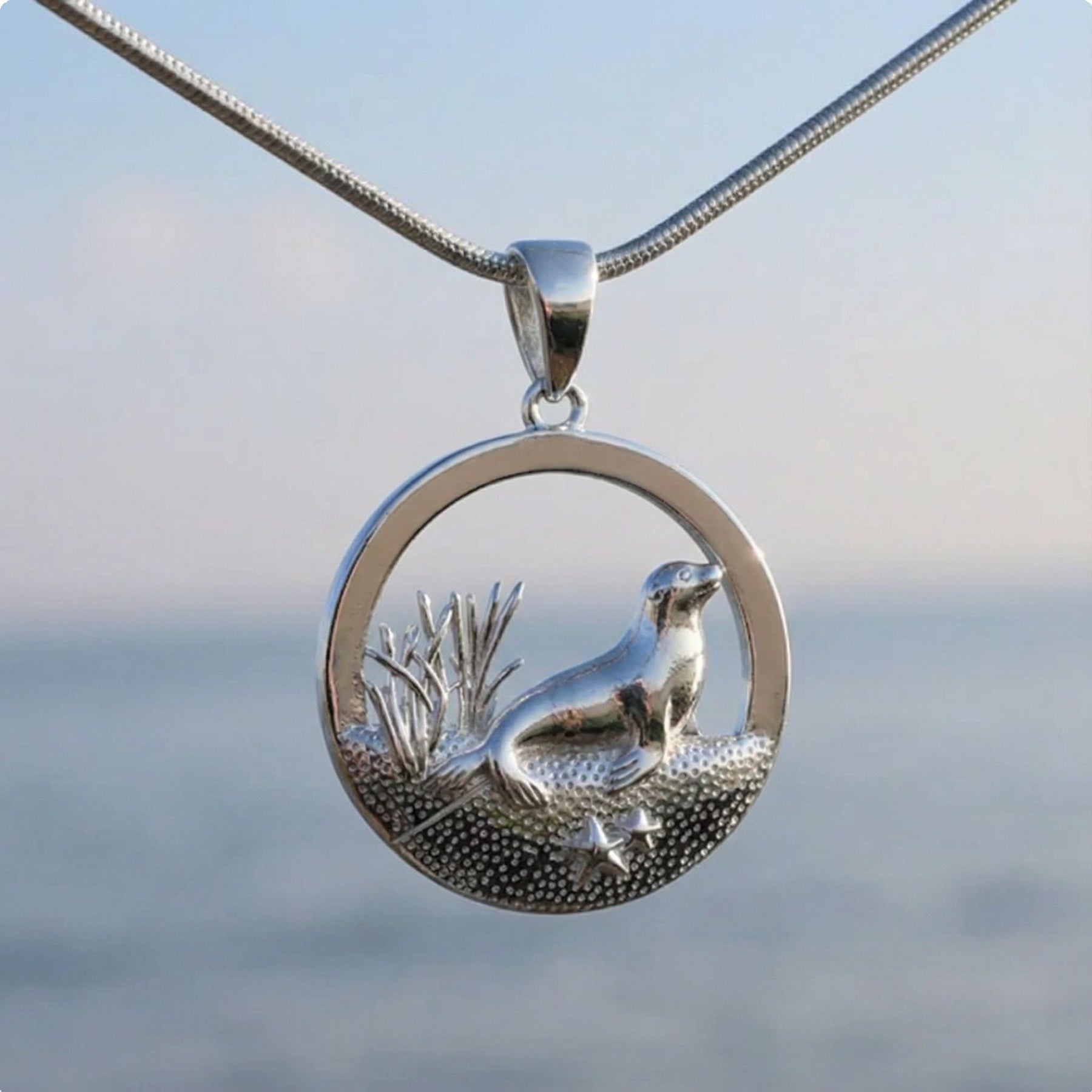 Silberner Seehund-Anhänger mit maritimem Motiv, Kette vor unscharfem Meer-Hintergrund