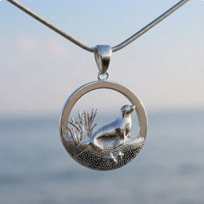 Silberner Seehund-Anhänger mit maritimem Motiv, Kette vor unscharfem Meer-Hintergrund