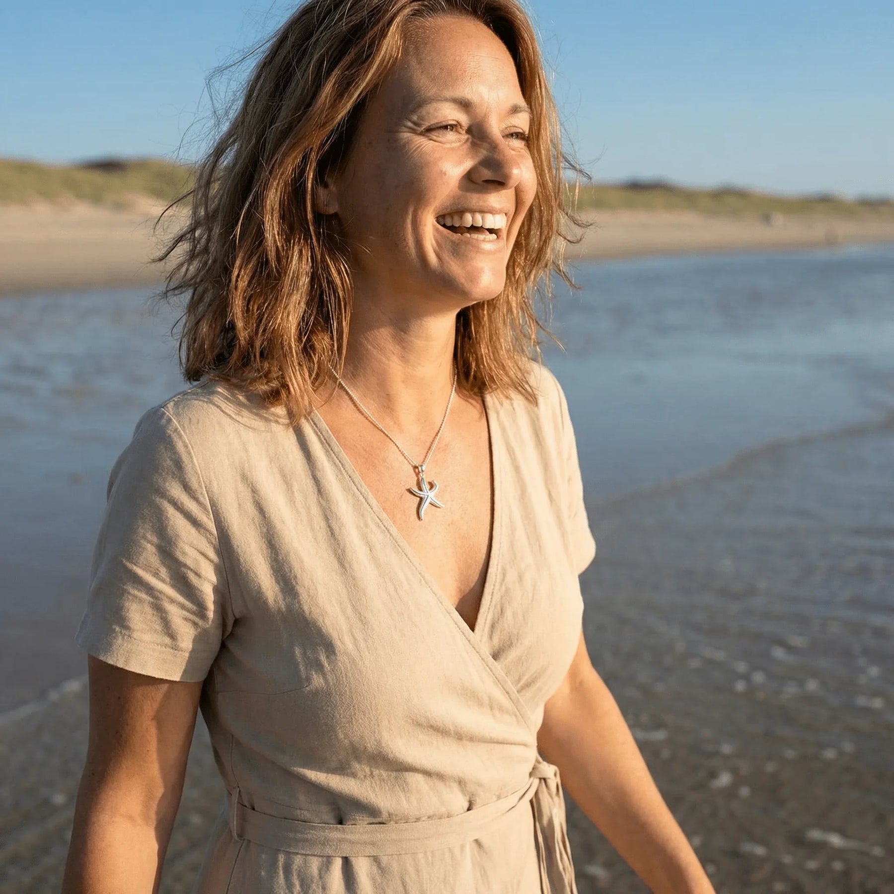 Frau am Strand mit silbernem Seestern-Anhänger, maritimer Schmuck im Sonnenlicht