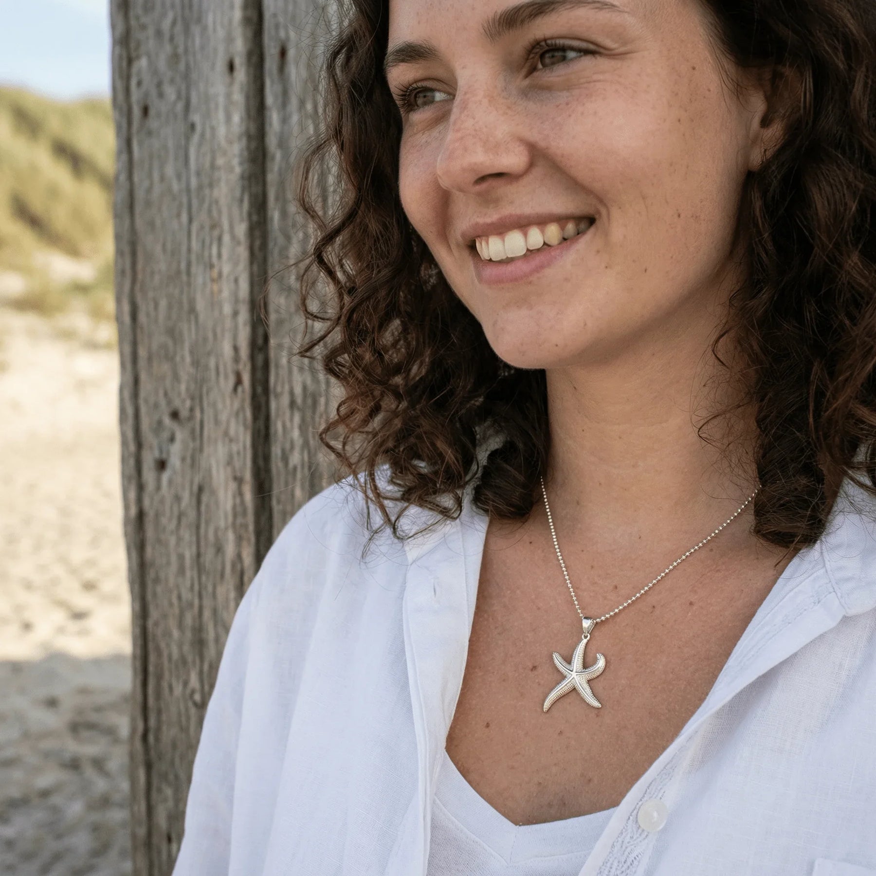 Frau am Strand trägt große Seestern-Kette aus Silber, maritimer Schmuck, Sommermode