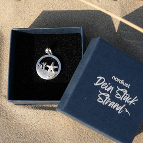 Silberner Seestern-Anhänger im runden Design auf Sand, maritime Schmuckverpackung