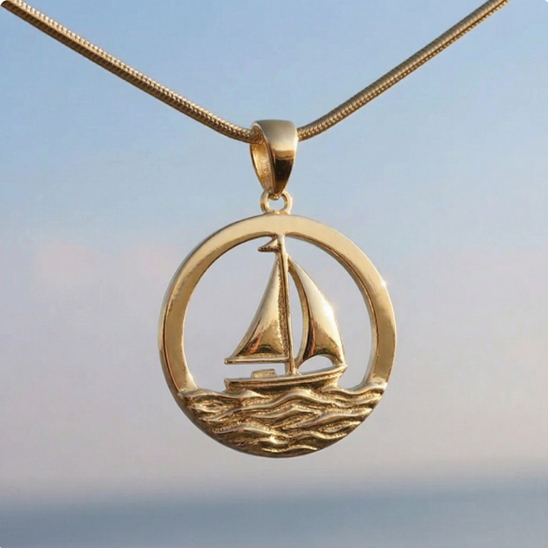 Goldener Kettenanhänger mit Segelschiff Motiv vor maritimem Hintergrund