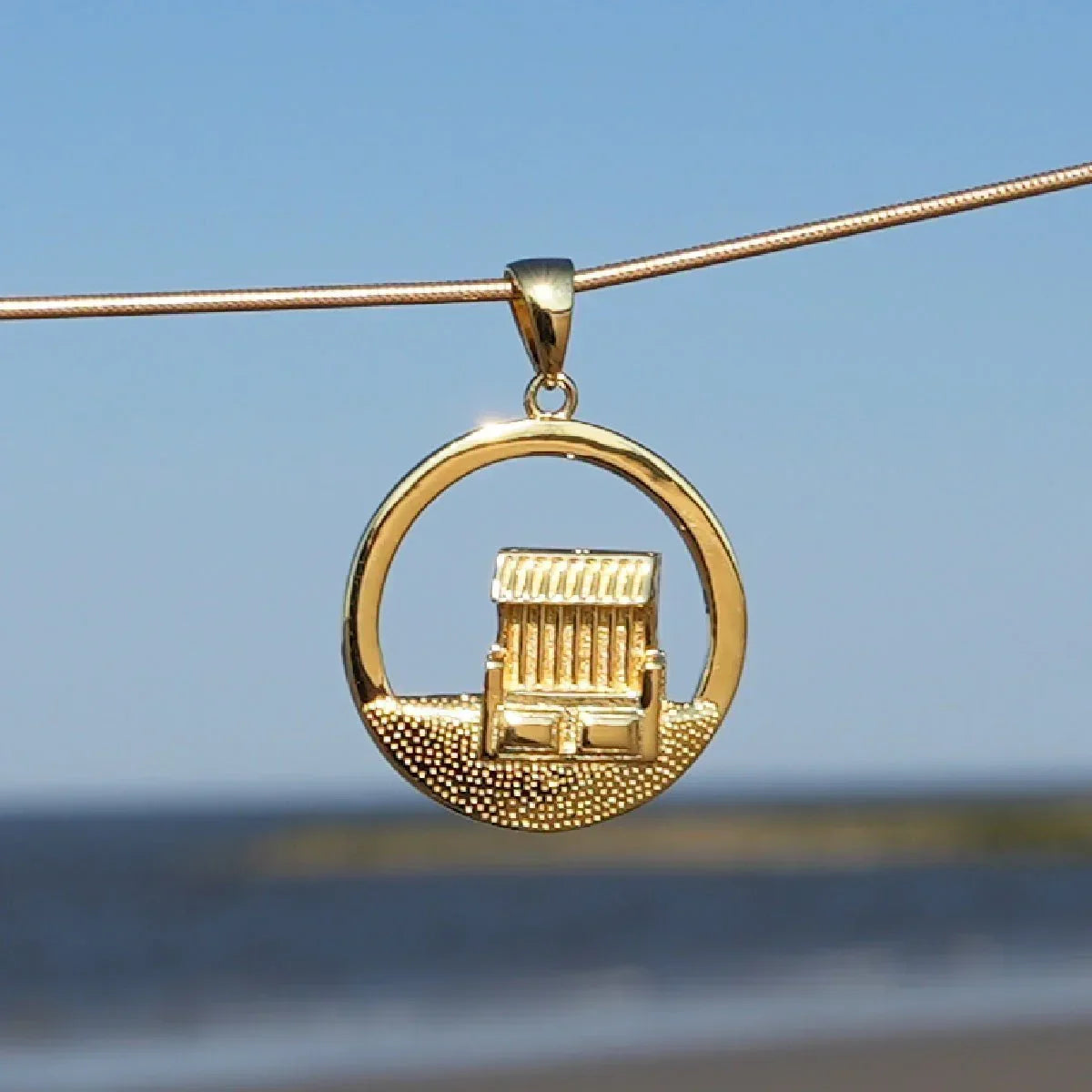 Goldener Anhänger mit Strandkorb-Motiv vor blauem Himmel und Meer