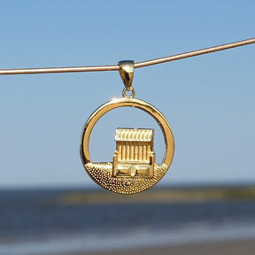Goldener Anhänger mit Strandkorb-Motiv vor blauem Himmel und Meer