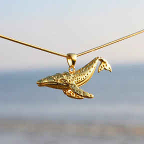 Goldene Wal-Kette als maritimer Schmuck vor unscharfem Strand-Hintergrund