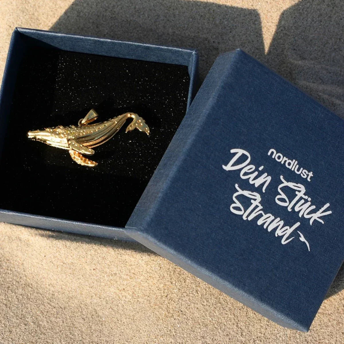 Vergoldeter Wal-Anhänger in Schmuckschachtel am Strand, maritimer Schmuck