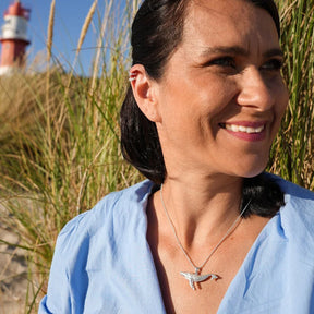 Frau mit silberner Wal-Kette am Strand, Leuchtturm im Hintergrund, maritimer Schmuck