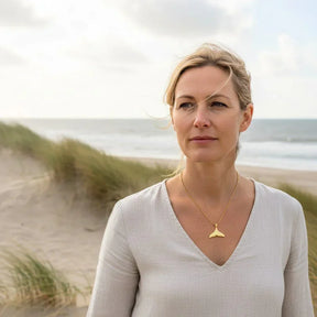 Frau mit goldener Walflossen-Kette am Strand, maritimer Schmuck, Naturkulisse