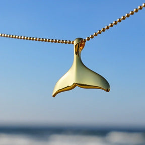 Goldene Walflossen-Kette vor blauem Himmel und Meer, maritimer Schmuck-Anhänger