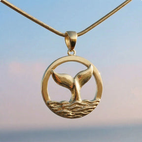 Maritane Halskette mit Walflosse Anhänger aus Metall, rund, vor blauem Himmel.