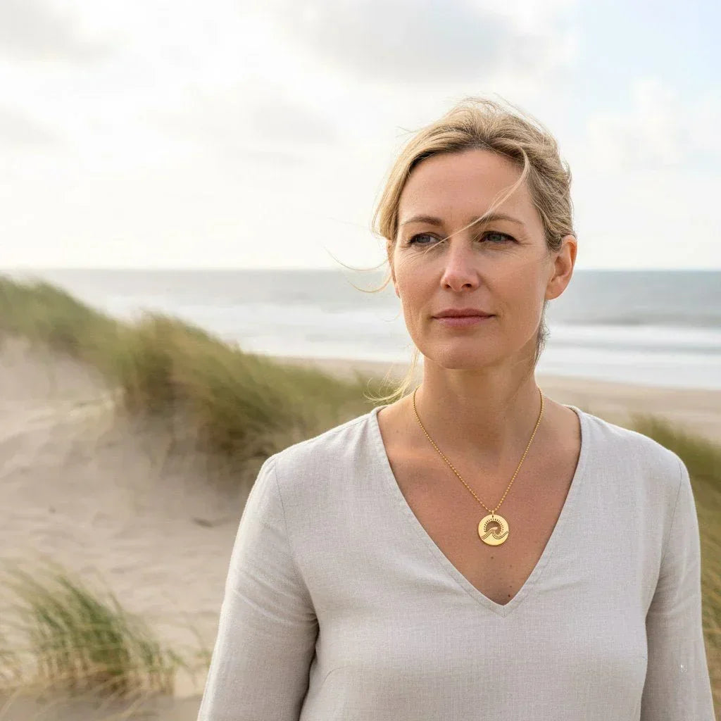 Frau am Strand mit goldener Wellen-Kette, maritimer Schmuck, Meerblick im Hintergrund
