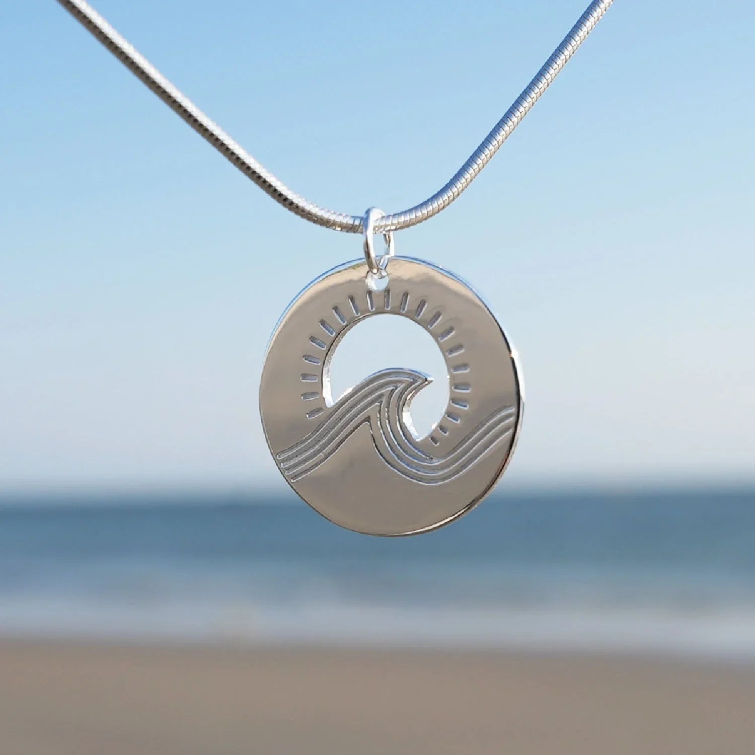 Silberne Halskette mit rundem Wellen-Anhänger am Strand, maritimer Schmuck
