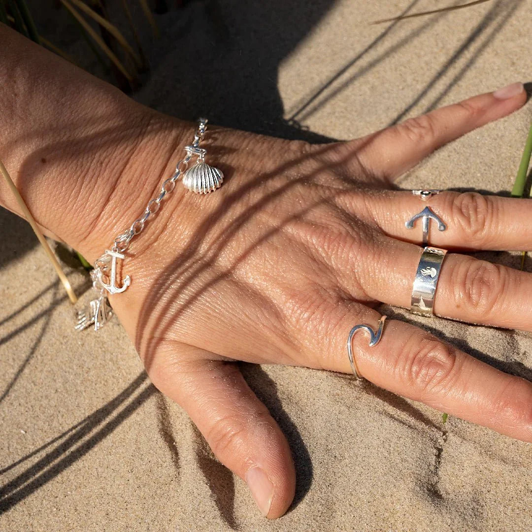 Hand mit maritimen Silberringen und Armband mit Anker und Muschel am Strand im Sand